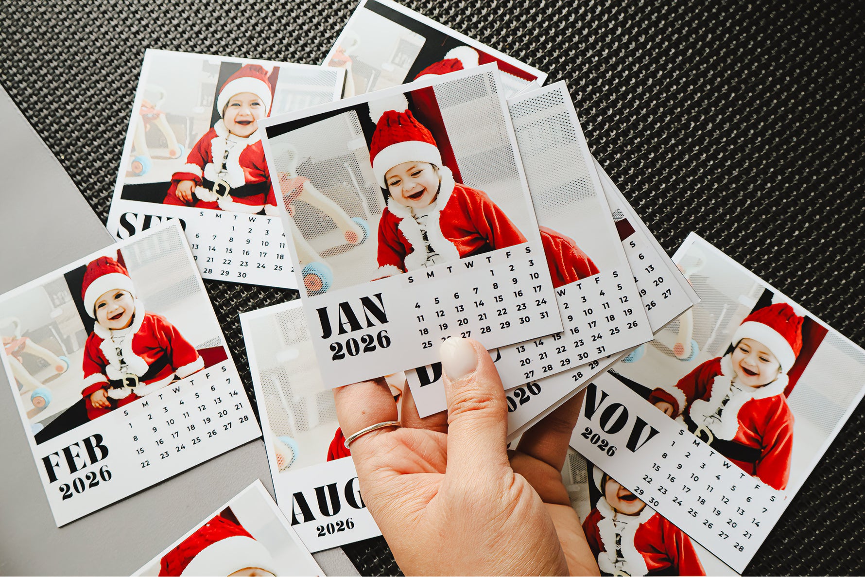 Calendar with a baby in a Santa hat held by a hand on a textured surface