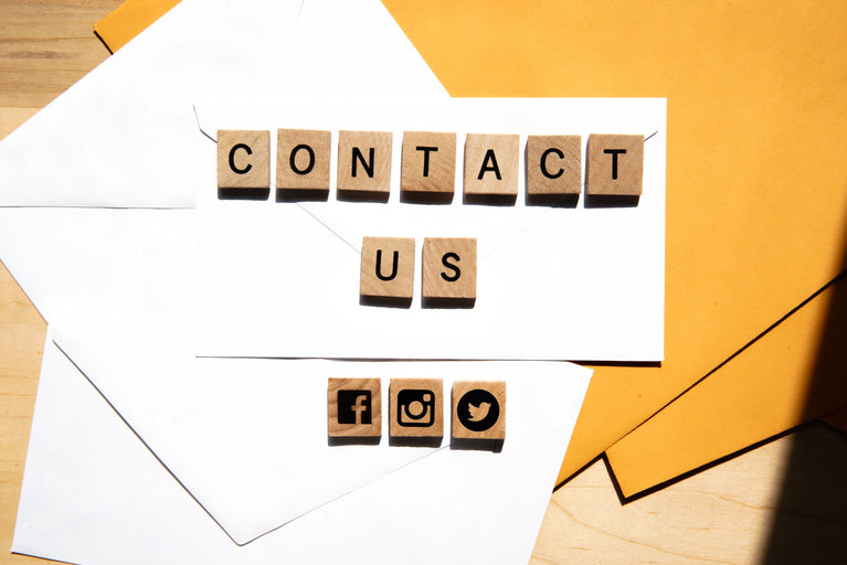 Contact us message spelled with wooden tiles on white envelopes, social media icons below